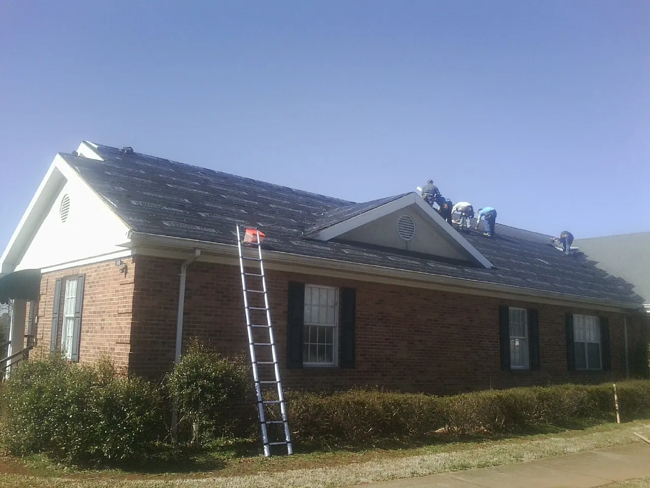 Crew tearing shingles off a brick ranch roof with a ladder set — Emergency Roof Repair work by our crew in Owenton