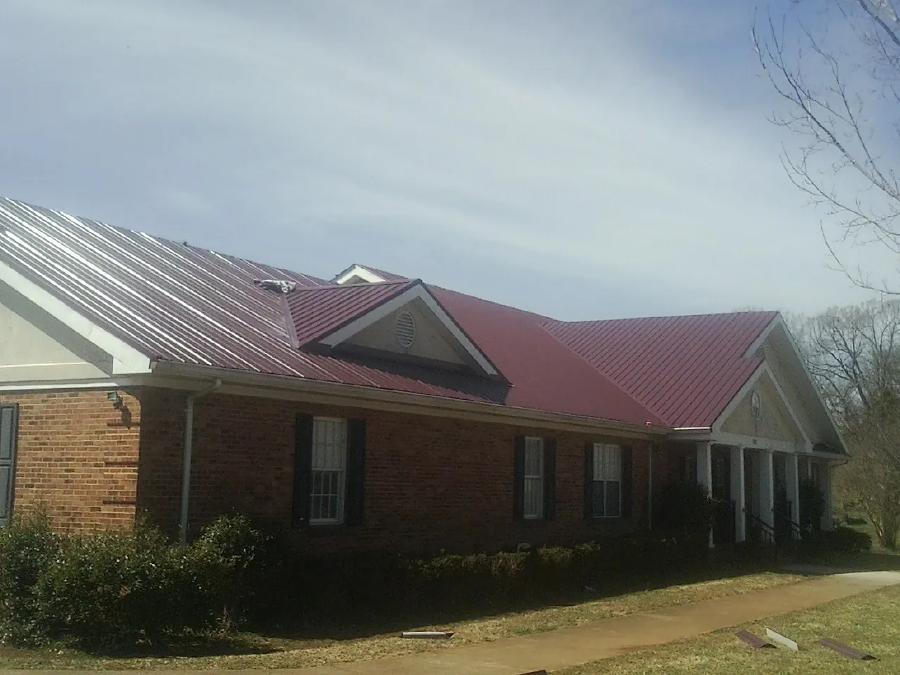 Red metal roof with gabled entries on a long brick building, from a Hail Damage Roof Repair job in Owenton