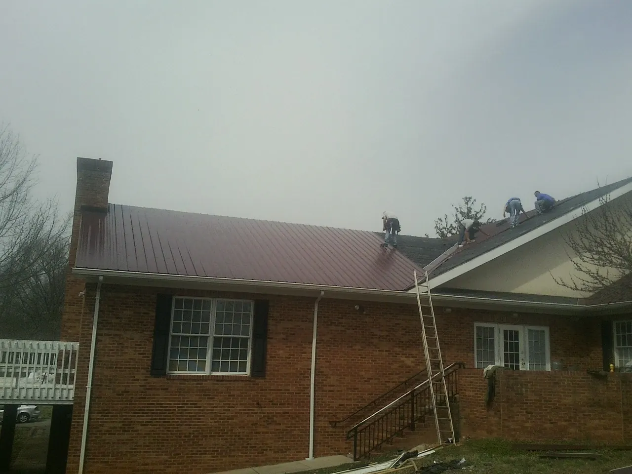 Crew setting red metal roofing panels on a brick home in Owenton