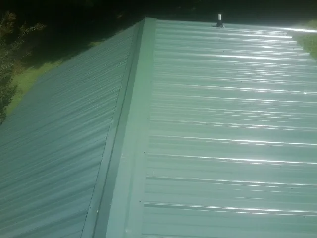 New green metal panels meeting at the ridge of a roof — Flat Roof Repair work by our crew in Owenton