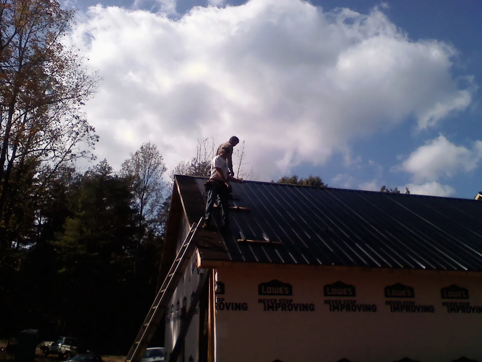 Roofer fastening dark metal panels high against a cloudy sky, from a Roof Inspection job in Owenton
