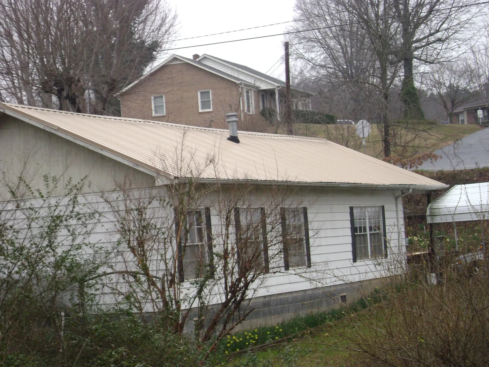 Tan metal roof on a white sided house set into a hillside — Commercial Roofing by Roofing Brothers in Owenton